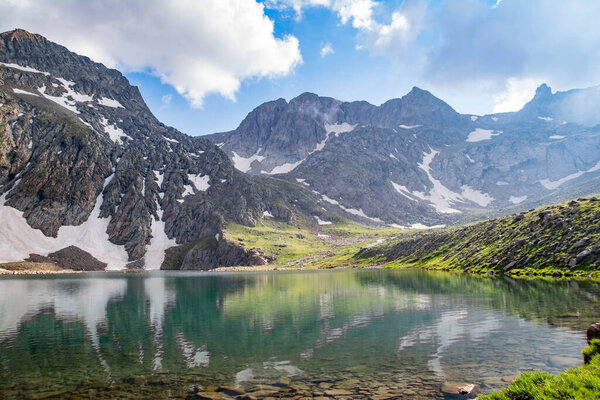 Горное озеро и скалистые горы. Кристально чистое озеро посреди скал. Зеленые поля, озера и горные хребты под снегом