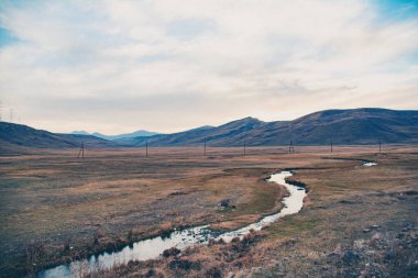Nehir tarlanın karşısına akar. Kayalar ve dağlarla güzel bir manzara.