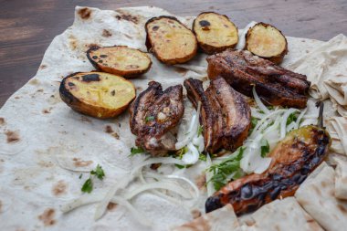 Kızarmış balık ve patates, siyah tabakta otlar ve sebzelerle..