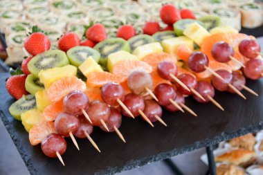 Siyah bir tabakta, şişte farklı meyveler. Bir tabakta kivi, mandalina, portakal, üzüm