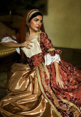 Young woman in medieval renaissance costume and French hood sitting on the floor holding a letter