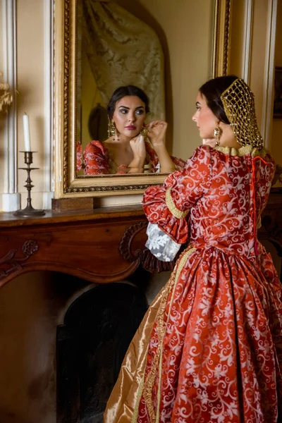 穿着复兴长袍的漂亮女人凝视着城堡里的一面古老的金镜 — 图库照片