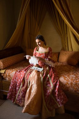 Renaissance lady in late medieval gown sitting on a beautiful canopy bed in her castle bedroom