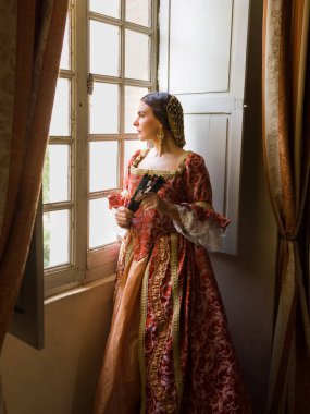 Otantik Rönesans kostümü ve başlık giymiş bir kadın ortaçağ şatosunun penceresinde dikiliyor.