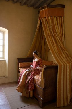 Renaissance lady in late medieval gown sitting on a beautiful canopy bed in her castle bedroom