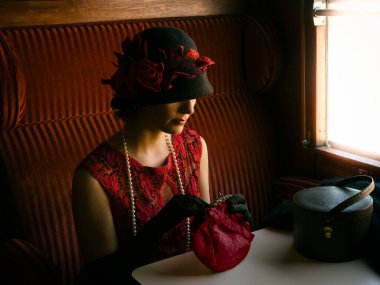 1927 model otantik bir buhar treninin içinde kırmızı flapper elbise ve saat şapkalı çekici bir kadın.