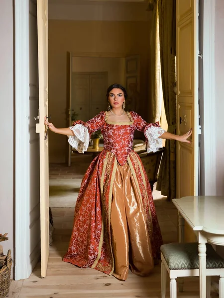 Beautiful woman in late renaissance costume posing between the open doors of a medieval castle.