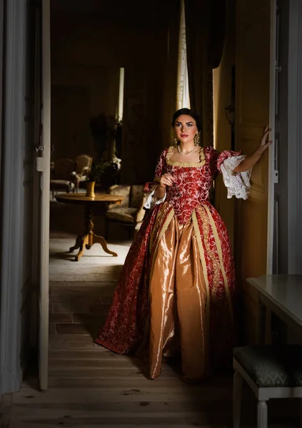 Beautiful woman in late renaissance costume posing between the open doors of a medieval castle.