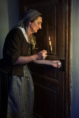 Lady in victorian costume holding a burning candle at the door