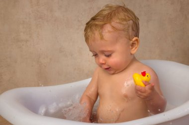 12 aylık küçük tatlı bir çocuğun mutlu sahneleri. Beyaz bir küvette oturmuş, su ve sabunla su sıçratıyor.