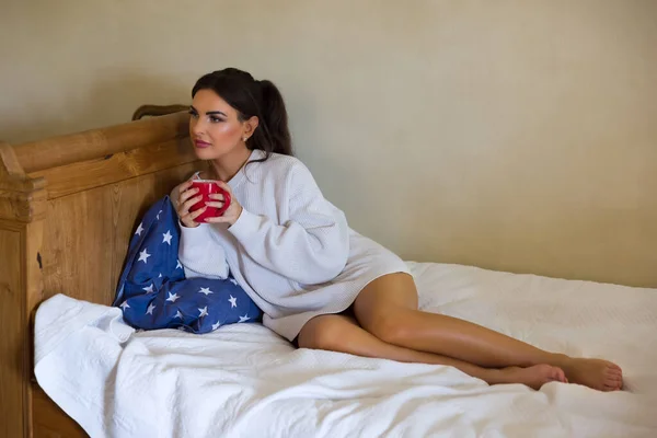 Attractive Young Woman Enjoying Mug Coffee Bed Wearing White Sweater — стоковое фото