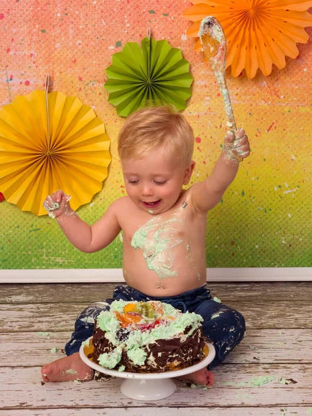 カラフルな画像間にザ 第一誕生日パーティーの小さなブロンド男の子Smashing彼の誕生日ケーキとともに木のスプーン — ストック写真