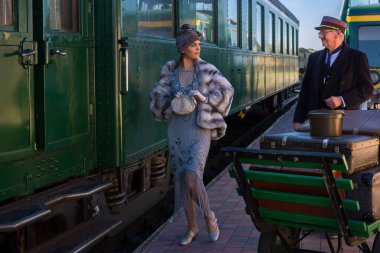 1927 model birinci sınıf bir tren vagonunun yanındaki platformda canlandırma sahnesinde 1920 'lerden kalma lüks bir bayan valizini bekliyor.