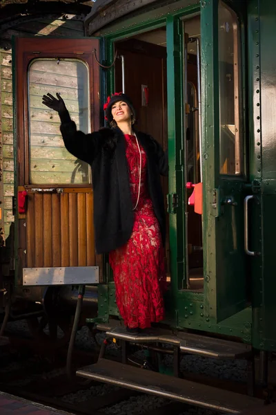 迷人的年轻女子 穿着20世纪20年代的红色连衣裙 头戴丁字裤帽 坐着老式蒸汽机车旅行 — 图库照片