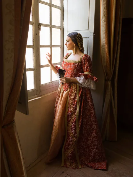 中世纪城堡里 一个女人站在窗前 头戴真实的文艺复兴式头饰和头饰 — 图库照片