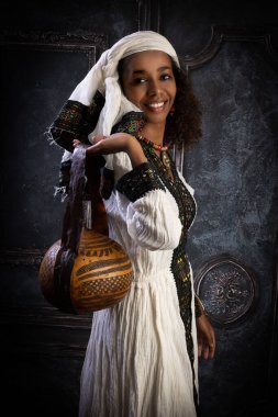 Geleneksel ulusal kostümüyle poz veren genç Etiyopyalı kadın içi boş bir su kabağından yapılmış bir çanta taşıyor.