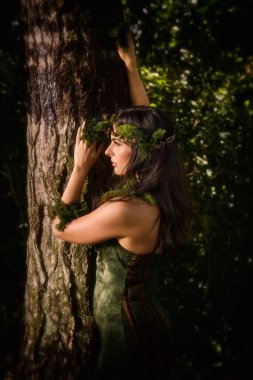 Yeşil elbiseli güzel genç bir kadın. Saf şifon kumaşları ve yosun çelenkleriyle orman perisi kılığına girmiş.