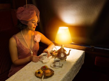1920 'lerden kalma şık elbiseli bir bayanın otantik bir 1927 model buhar treninin kompartımanında çay içişini canlandırma sahnesi.