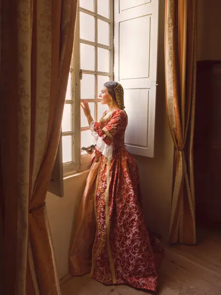 中世纪城堡里 一个女人站在窗前 头戴真实的文艺复兴式头饰和头饰 — 图库照片