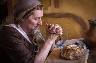 Hakiki köylü rönesans kostümü giymiş bir kadın masada dua ediyor. Masada ekmek var..