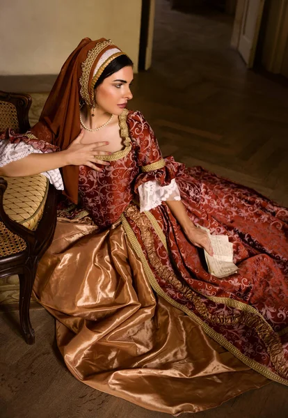 Young woman in medieval renaissance costume and French hood sitting on the floor holding a letter