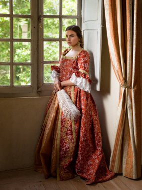 Otantik Rönesans kostümü ve başlık giymiş bir kadın ortaçağ şatosunun penceresinde dikiliyor.