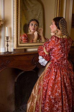 Rönesans elbisesi içindeki güzel kadın kalesindeki antik altın aynaya bakıyor.