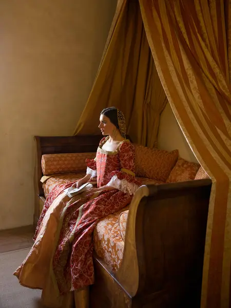 Renaissance lady in late medieval gown sitting on a beautiful canopy bed in her castle bedroom