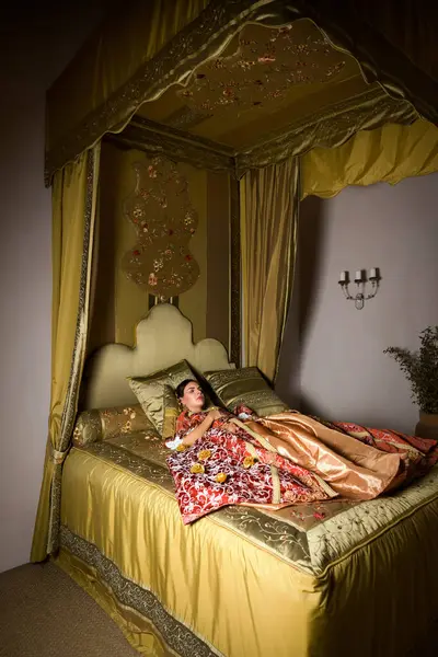 Altın ortaçağ yatak odası ve güzel bir yatak örtüsü. Rönesans elbisesi giymiş bir kadın Cinderella tarzında uzanıyor..