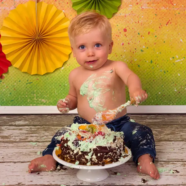 カラフルな画像間にザ 第一誕生日パーティーの小さなブロンド男の子Smashing彼の誕生日ケーキとともに木のスプーン ロイヤリティフリーのストック画像
