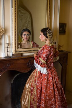 Rönesans elbisesi içindeki güzel kadın kalesindeki antik altın aynaya bakıyor.