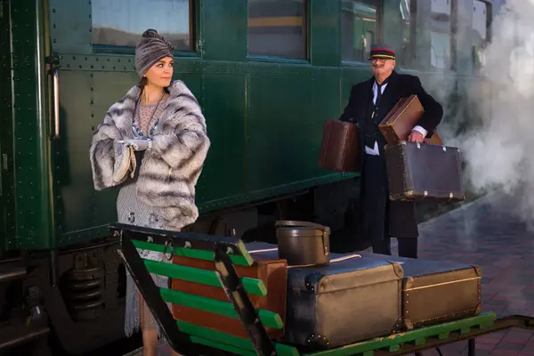 本物の1927ファーストクラスの電車ワゴンの近くのプラットフォーム上の再現シーンでは 1920年代の女性が荷物を待っています ストック写真