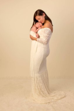 Beyaz dantelli bir elbise içindeki güzel anne, 7 günlük oğluyla poz veriyor.
