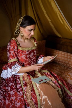 Renaissance lady in late medieval gown sitting on a beautiful canopy bed in her castle bedroom