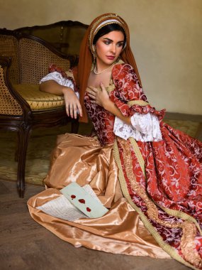 Young woman in medieval renaissance costume and French hood sitting on the floor holding a letter