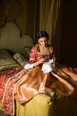 Altın ortaçağ yatak odası ve güzel bir yatak örtüsü. Rönesans elbiseli bir bayan nakış işliyor..