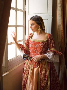 Otantik Rönesans kostümü ve başlık giymiş bir kadın ortaçağ şatosunun penceresinde dikiliyor.