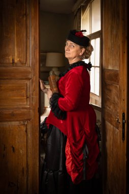 Kırmızı ve siyah kadife kadife elbiseli kadın 18. yüzyılda iç mekanda poz vermiş.