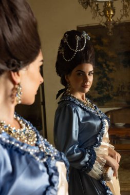Rokoko kraliçesi Marie Antoinette tarzı giyinmiş ve Fransız şatosunun iç kısımlarında otantik bir peruk takmış güzel bir kadın.