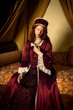 Bir Rönesans Kraliçesi 'nin canlandırma sahneleri. Tudor tarzında. Bir Fransız şatosunda antik bir yatak üzerinde poz veriyor.