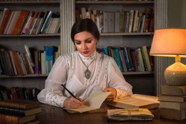 Kütüphanede oturan Edwardian etekli ve yüksek yakalı dantel bluzlu güzel bayan. Öğretmen de olabilir, müdire de..