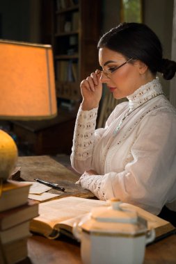 Beautiful lady in Edwardian skirt and high collar lace blouse sitting in the library. She could be a teacher or even a headmistress. clipart