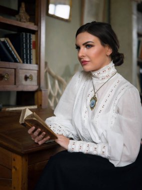 Kütüphanede oturan Edwardian etekli ve yüksek yakalı dantel bluzlu güzel bayan. Öğretmen de olabilir, müdire de..