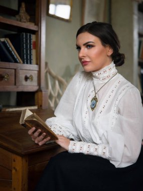 Beautiful lady in Edwardian skirt and high collar lace blouse sitting in the library. She could be a teacher or even a headmistress. clipart