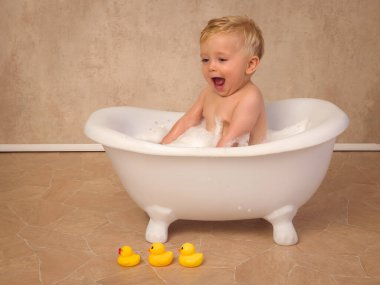 12 aylık küçük tatlı bir çocuğun mutlu sahneleri. Beyaz bir küvette oturmuş, su ve sabunla su sıçratıyor.