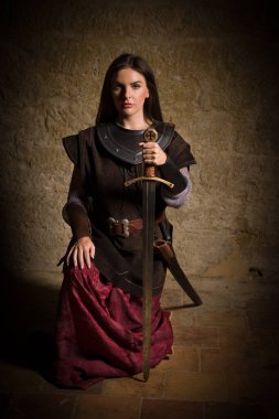 Genç bir kadın ortaçağ şövalyesini canlandırıyor. Deri ceket ve metal zırh giyiyor. Joan of Arc tarzında.