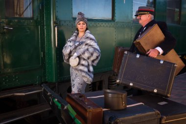 1927 model birinci sınıf bir tren vagonunun yanındaki platformda canlandırma sahnesinde 1920 'lerden kalma lüks bir bayan valizini bekliyor.