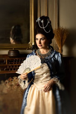 Rokoko kraliçesi Marie Antoinette tarzı giyinmiş ve Fransız şatosunun iç kısımlarında otantik bir peruk takmış güzel bir kadın.
