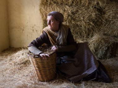 Tarihi ortaçağ kostümlü bir kadın saman ambarında hasır sepeti ile poz veriyor.