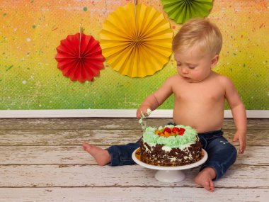 İlk doğum günü partisinde çekilen renkli görüntüler. Küçük sarışın bir çocuk doğum günü pastasını tahta kaşıklarla eziyor.